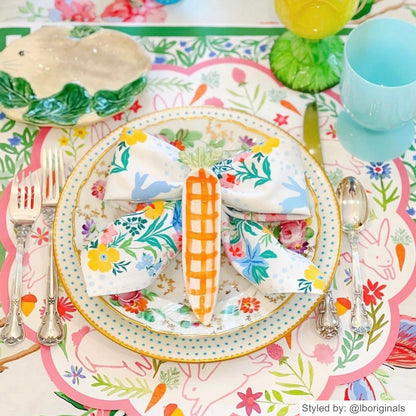 Easter place setting with a bunny scalloped round paper placemat layered with china and a floral napkin tied into a bow with a carrot shaped dish on top